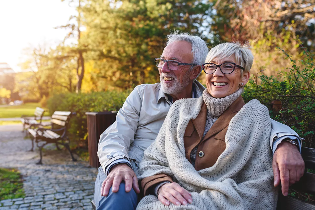Smiling senior couple sitting on the bench in the park together enjoying retirement